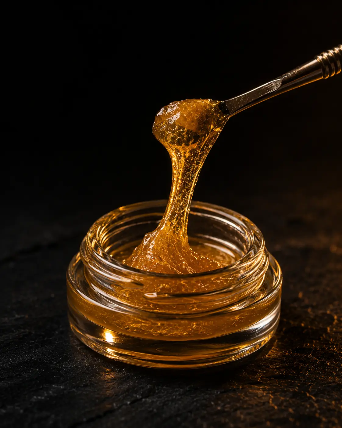 Dab tool lifting golden cannabis concentrate from a glass jar